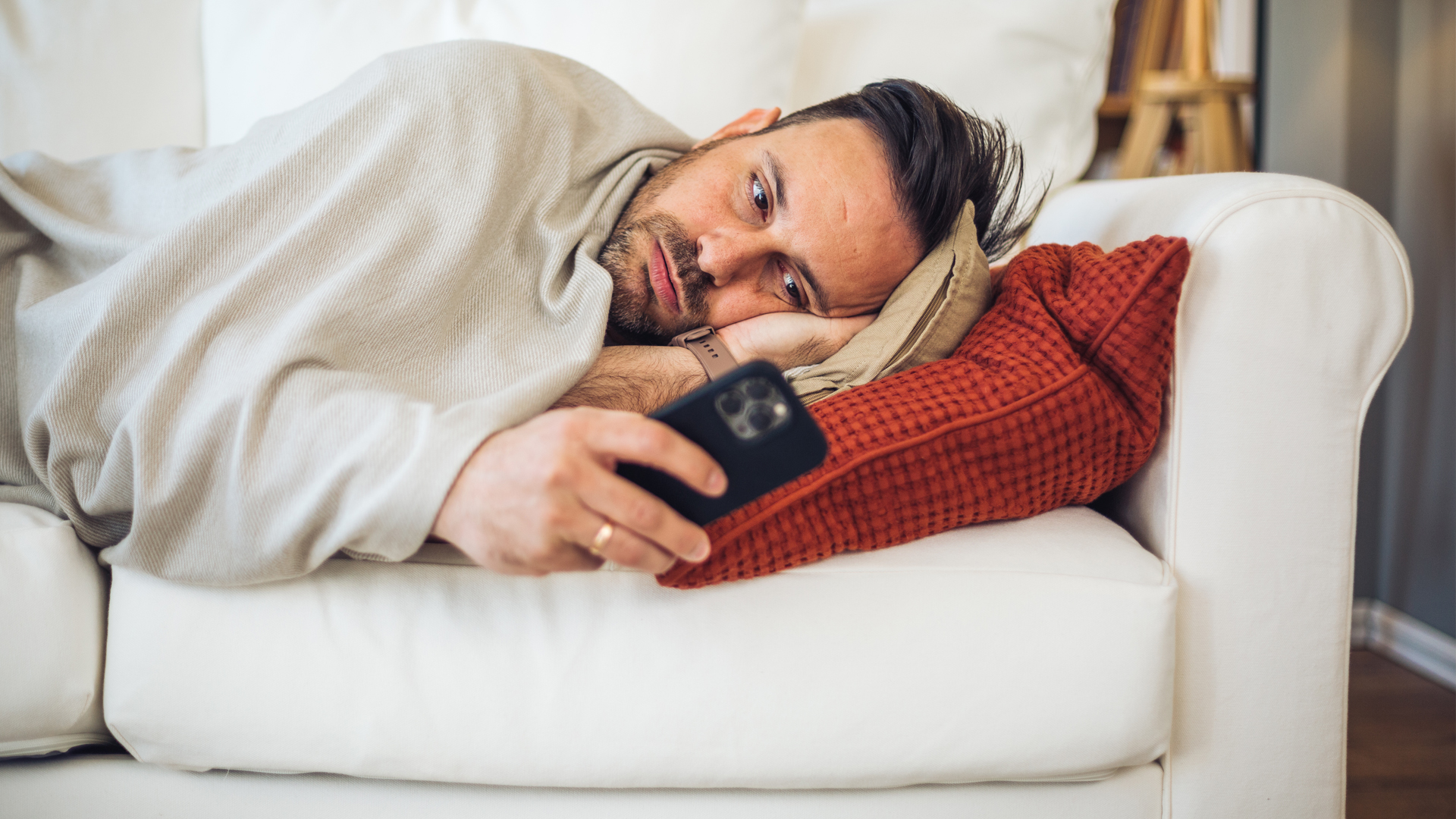 Un homme est allongé dans son lit et utilise son smartphone pour vérifier ses symptômes en ligne.