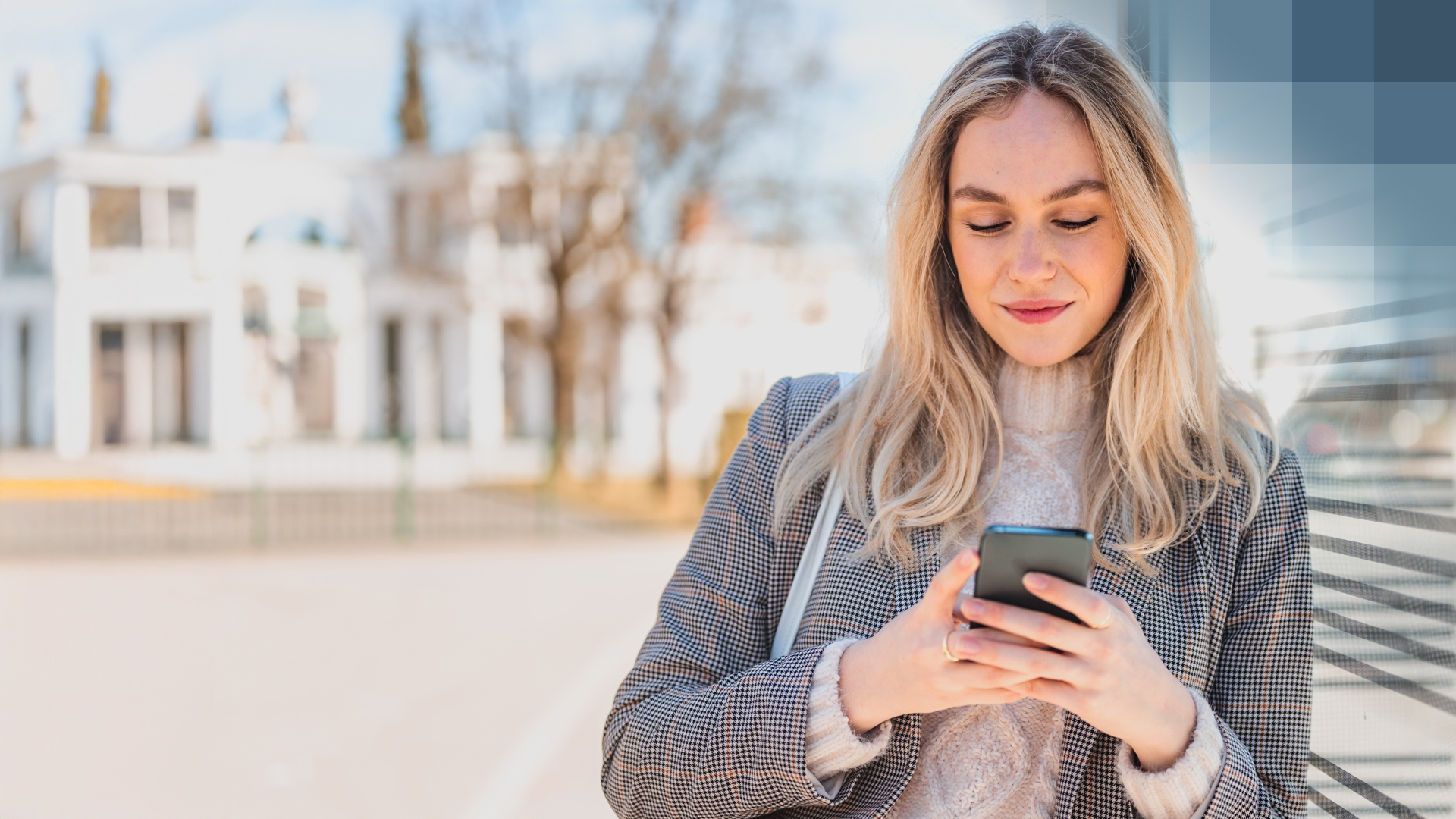 Une jeune femme en blazer regarde son smartphone et se renseigne sur l'assurance semi-privée.