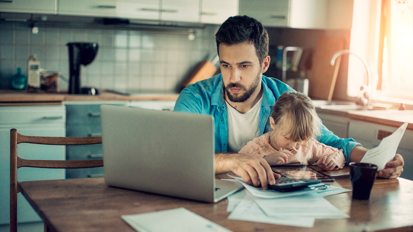 Un père est assis à table avec sa fille et cherche sur son ordinateur comment économiser sur les primes d’assurance maladie.