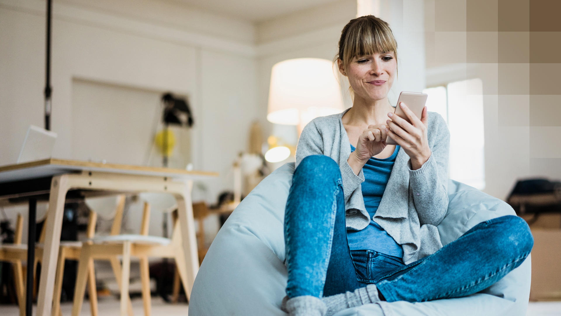 Une jeune femme est assise sur un canapé et s'inscrit à la newsletter de la KPT sur son téléphone portable.