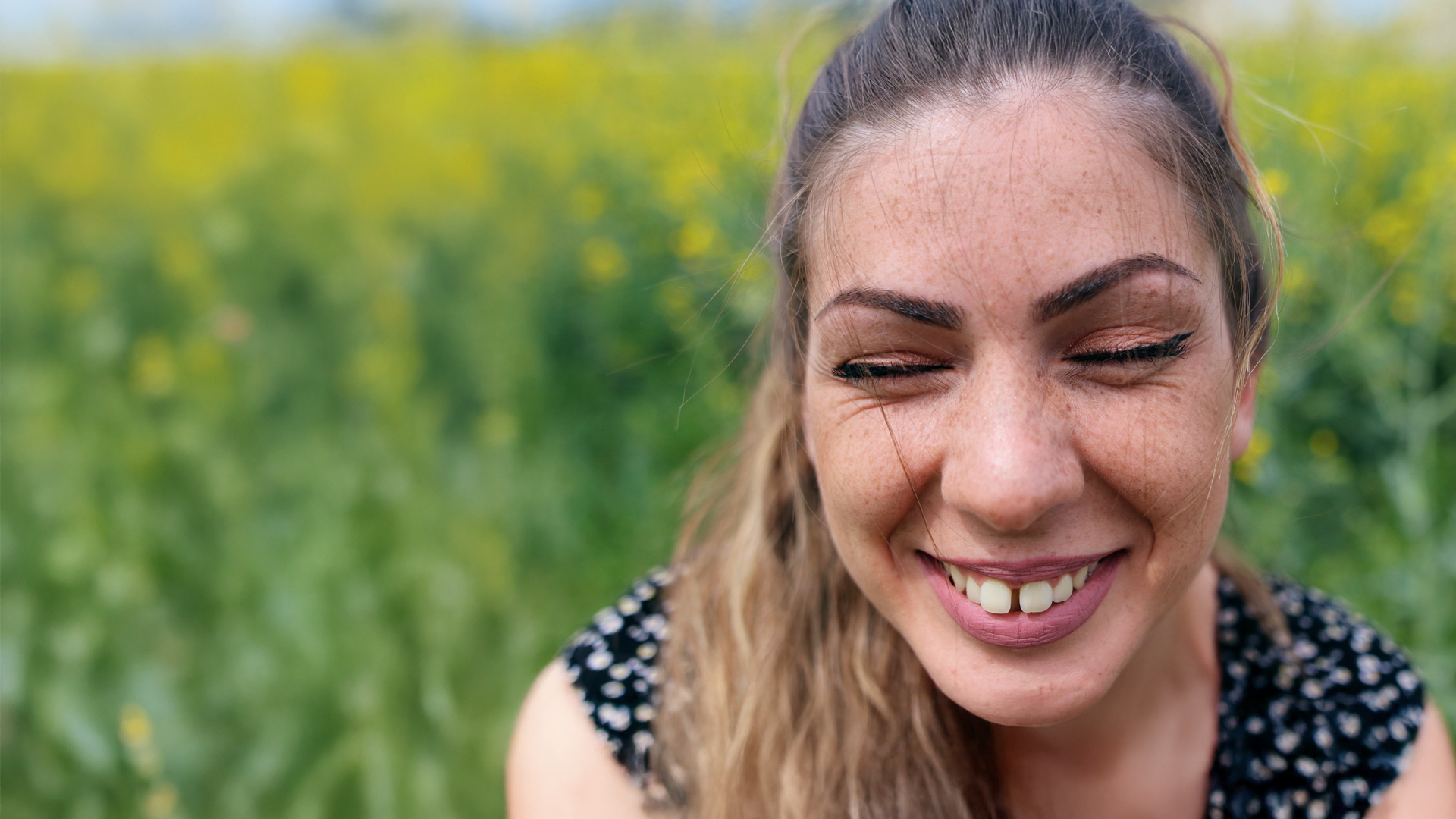 Une jeune femme aux longs cheveux bruns et aux taches de rousseur rit les yeux fermés, révélant son diastème entre les dents de devant.