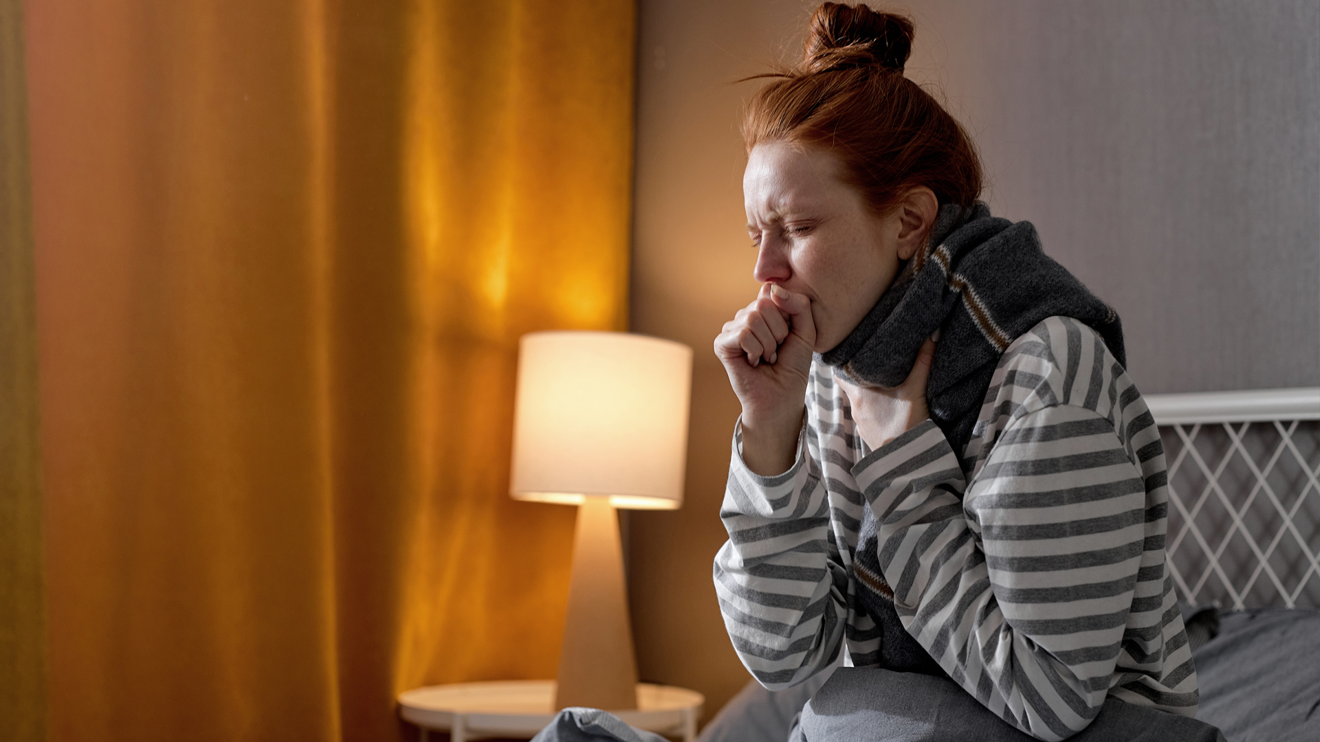 Une femme malade assise dans son lit et toussant à cause d'une angine