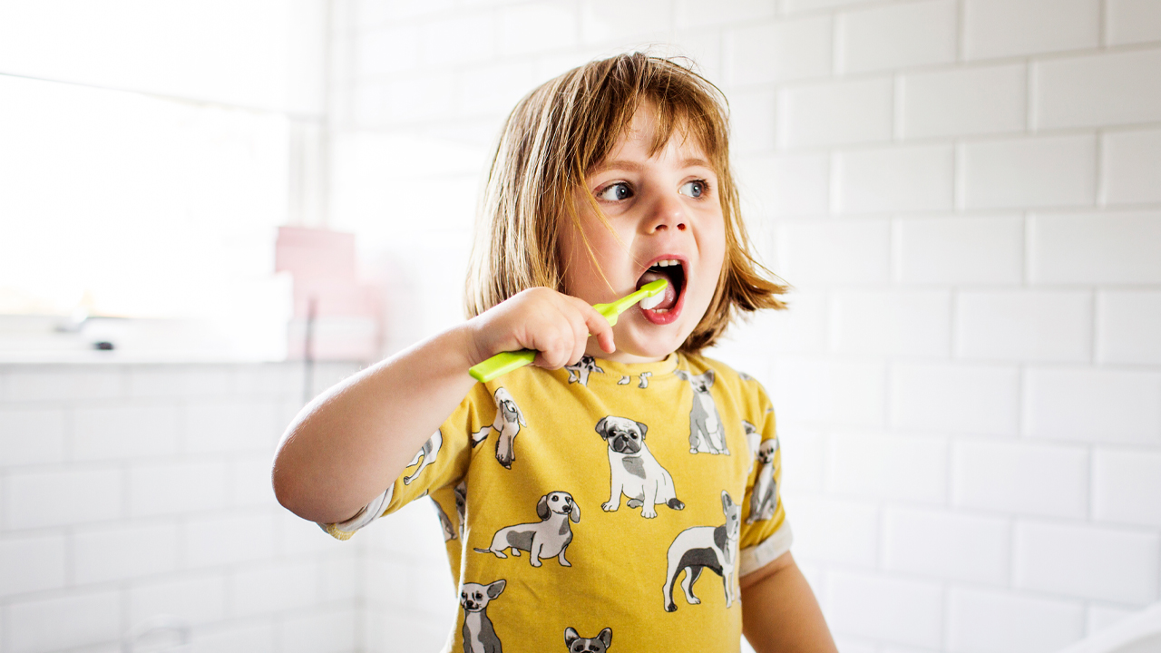 Un jeune enfant se brosse les dents dans la salle de bains avec une brosse à dents verte.