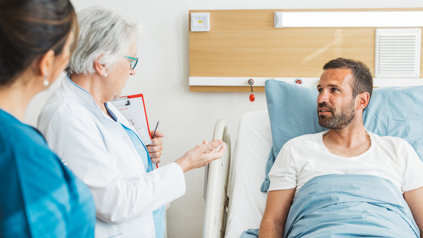 Un homme est allongé dans un lit d’hôpital et écoute sa médecin lui expliquer les avantages de l’assurance semi-privée.