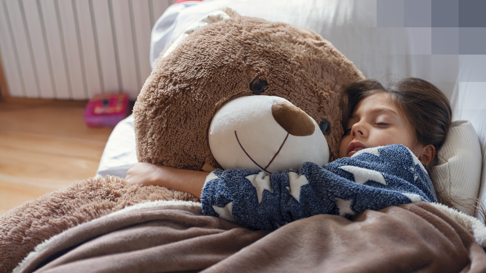 Une jeune fille dort dans son lit en serrant son grand ours en peluche et est heureuse d’être protégée par une assurance pour enfants.