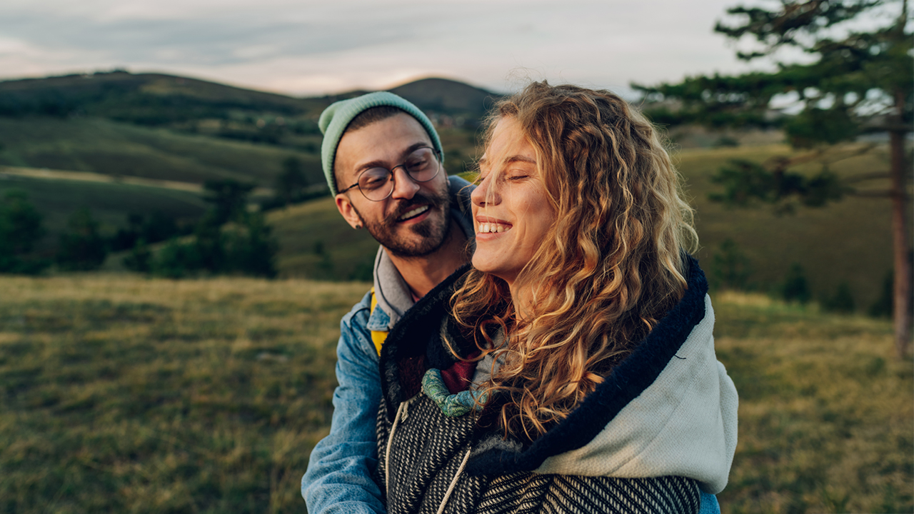 Un jeune couple se tient dehors dans la nature, se serre dans les bras et est heureux d’être en bonne santé grâce au modèle HMO.