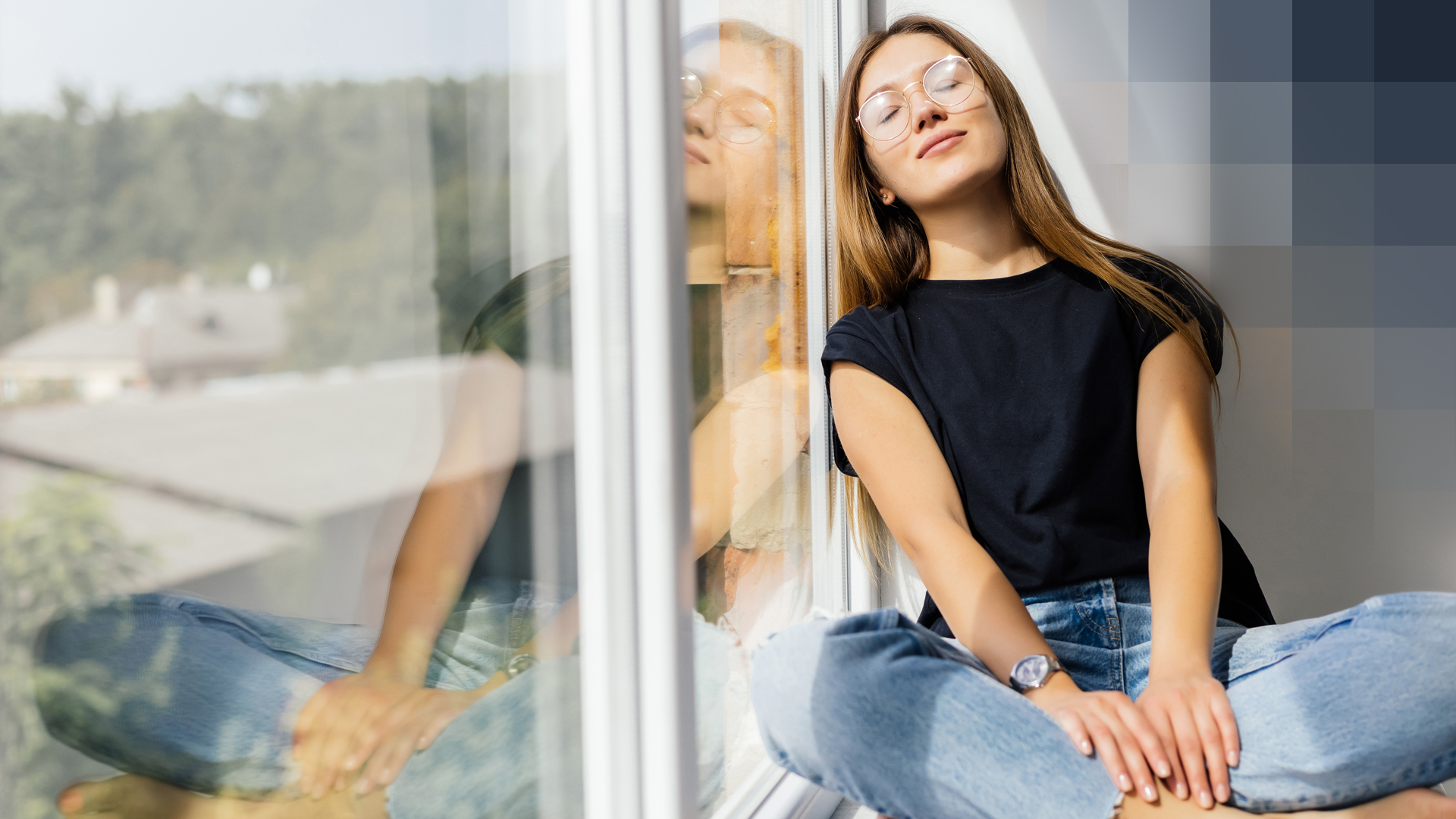 Une jeune femme avec des lunettes est assise près d’une grande fenêtre, ferme les yeux et est heureuse de son assurance complementaire d'hospitalisation..