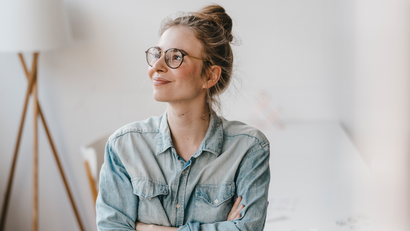 Une femme portant une chemise et des lunettes sourit, heureuse des prestations de sa caisse maladie pour ses lunettes.