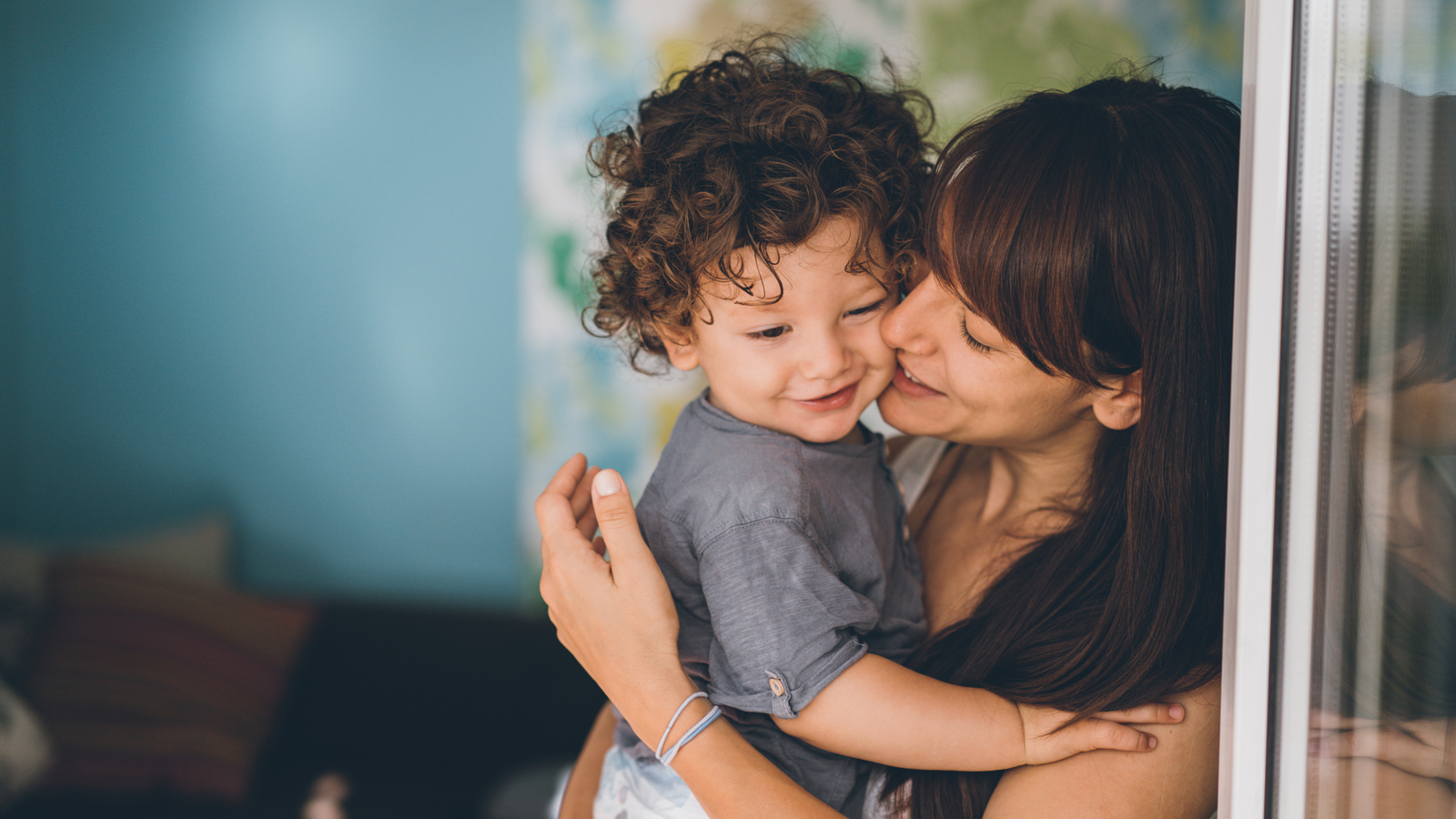 Une jeune mère sourit en tenant son enfant dans ses bras et se sent bien protégée grâce à son assurance complémentaire pour enfants.