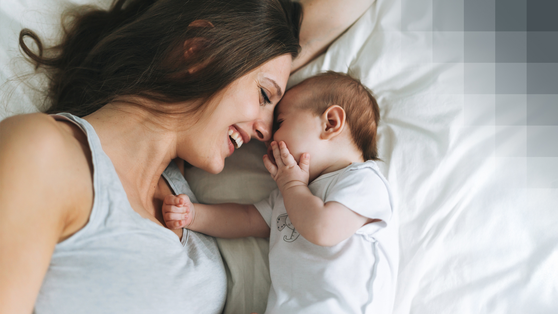 A smiling woman lying on a bed with her baby, happy to have completed the prenatal registration in good time.