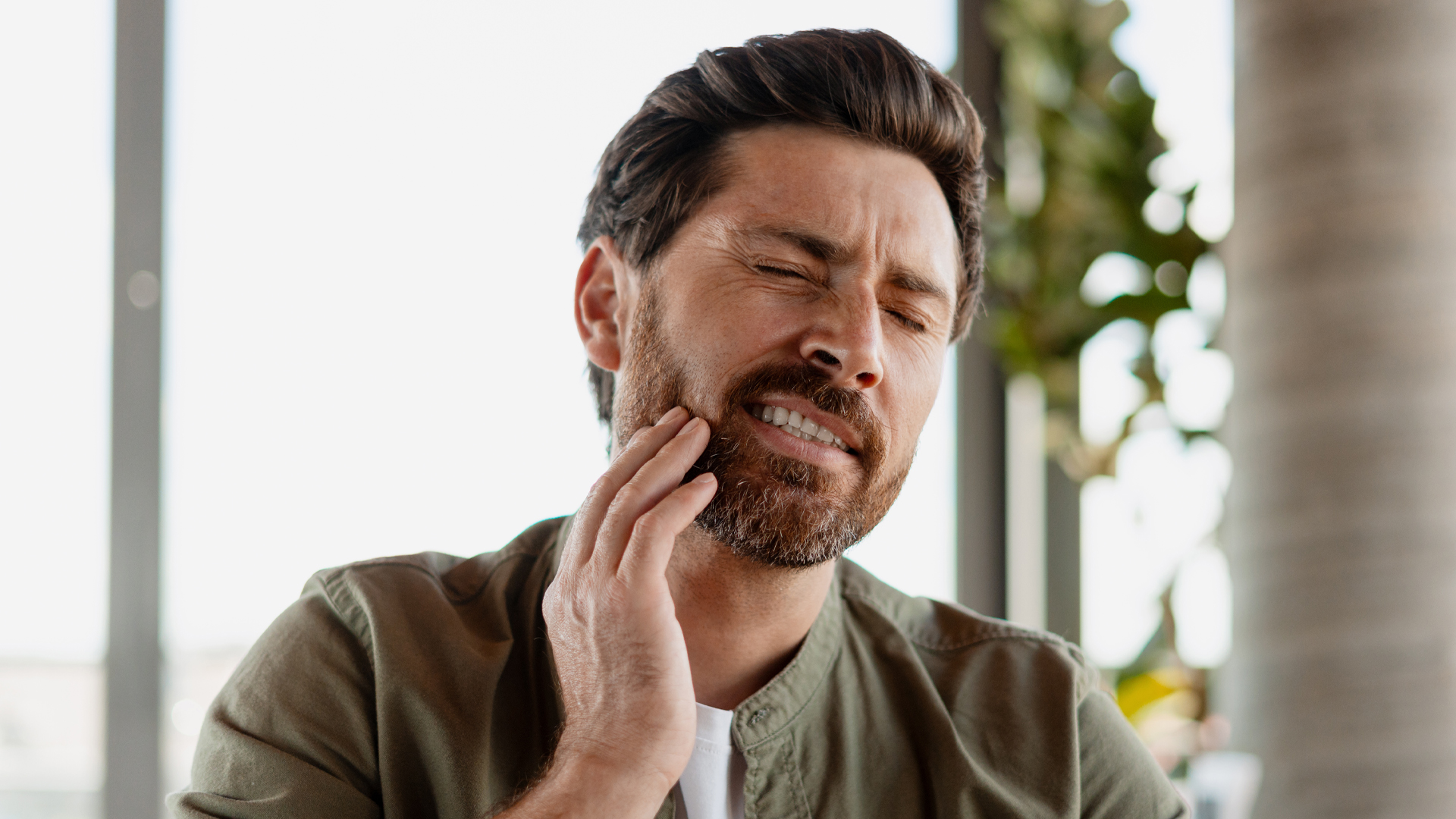 Gros plan d’un homme serrant les dents et se tenant la mâchoire en raison de douleurs liées au bruxisme.