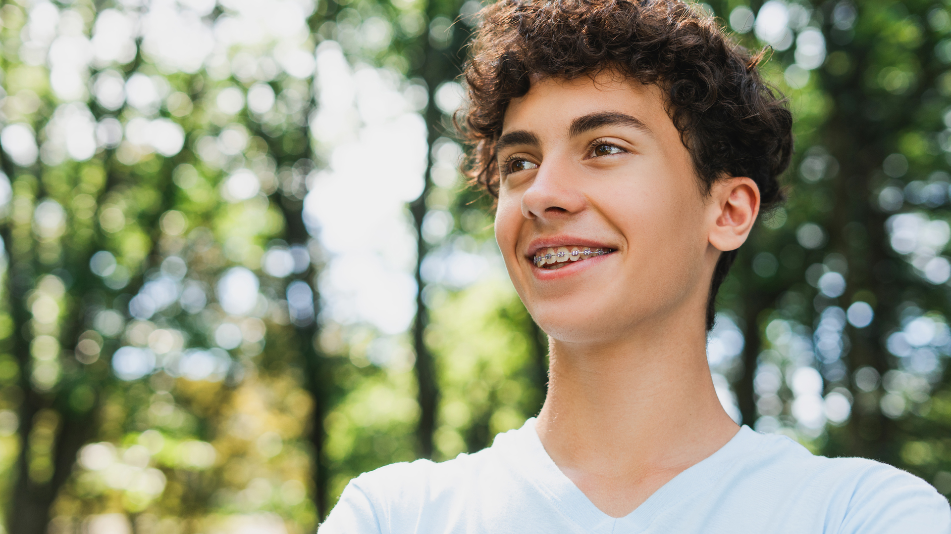 A boy wearing a white T-shirt smiles and shows his tooth brackets.