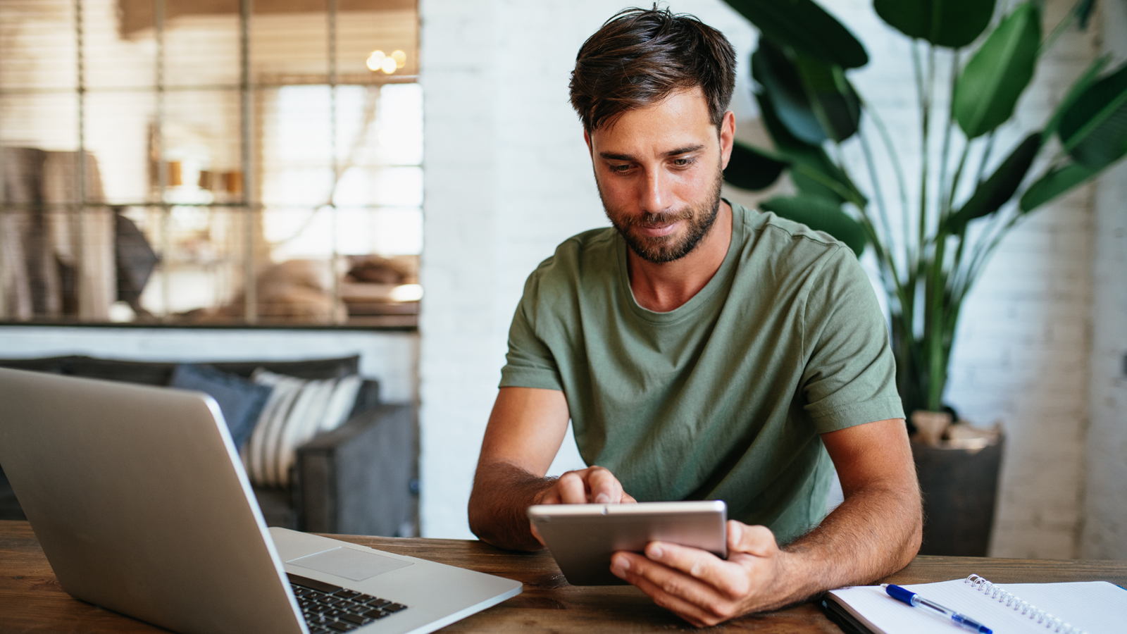 Un homme, pensif, est assis devant son ordinateur portable et sa tablette pour s’informer sur les examens de prévention en Suisse.